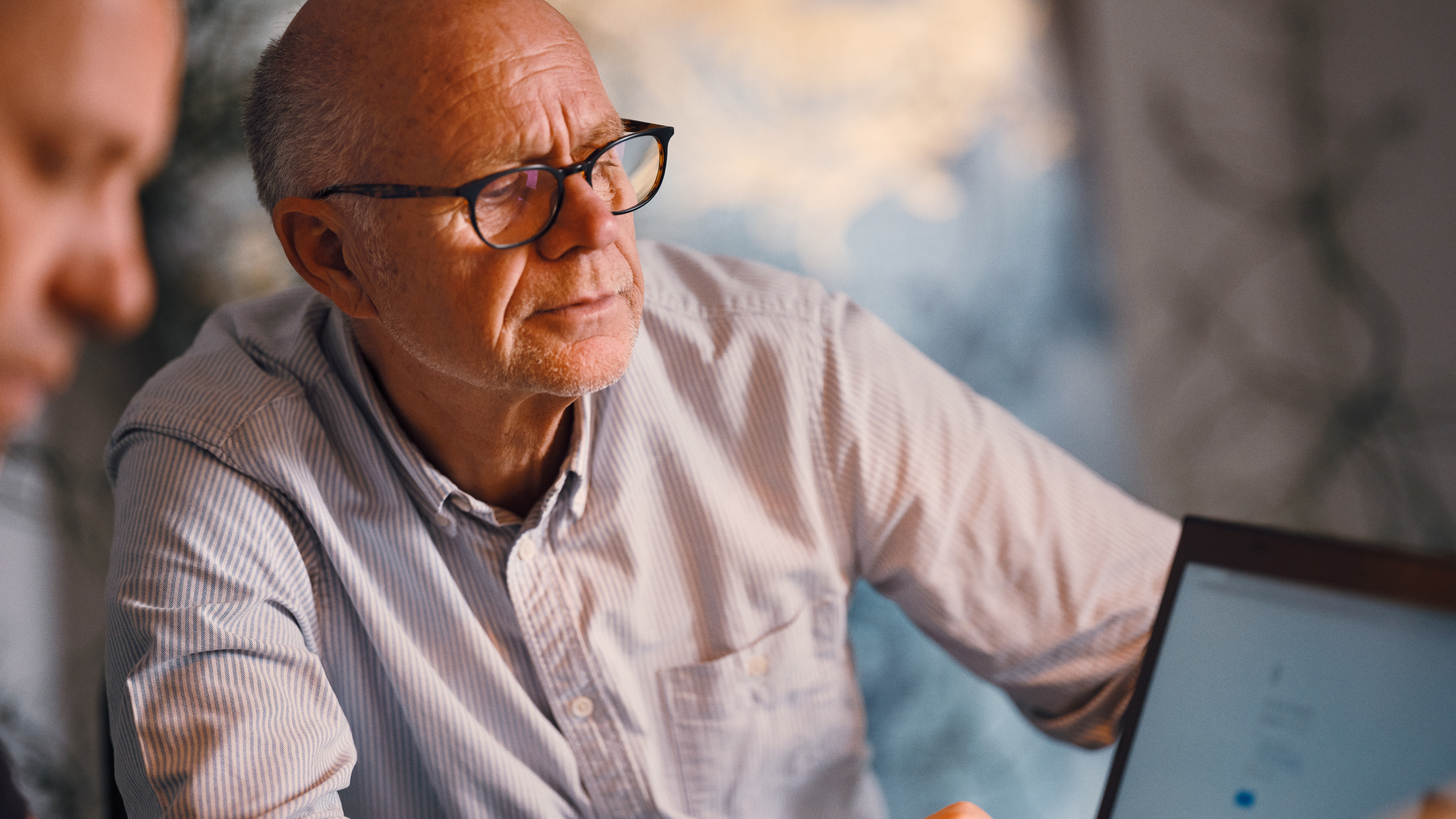 Ældre mand sidder med sin pensionsrågiver og modtager rådgivning på en computer om sin pensionsopsparing